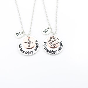 May include: Two silver necklaces with matching pendants. The pendants are round and have the words "no matter where" and "no matter when" engraved on them. One pendant features a compass and the other features a sun, moon, and stars.