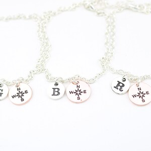 May include: Three silver chain bracelets with charms. Each bracelet has a compass charm and a letter charm. The letters are G, B, and R.
