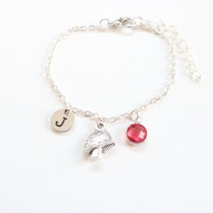 May include: A silver chain bracelet with a mushroom charm, a red gemstone charm, and a silver charm with the letter "J" on it.