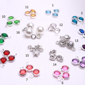 May include: Assortment of 16 silver charm pendants with various colored crystal stones. The charms feature different shapes, including hearts, stars, and circles.