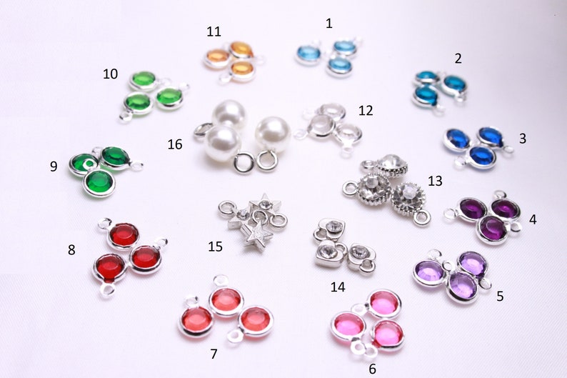 May include: Assortment of 16 silver charm pendants with various colored crystal stones. The charms feature different shapes, including hearts, stars, and circles.