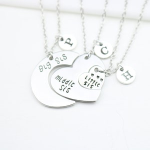 May include: Three silver necklaces with charms that say "Big Sis", "Middle Sis", and "Little Sis". Each necklace also has a charm with a letter on it.