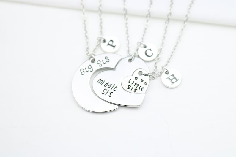 May include: Three silver necklaces with charms that say "Big Sis", "Middle Sis", and "Little Sis". Each necklace also has a charm with a letter on it.