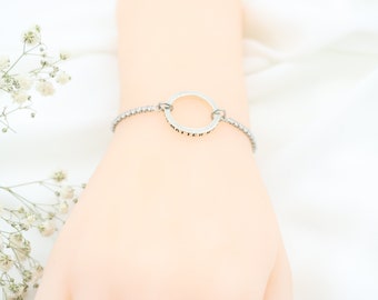 Peut inclure: Un bracelet argenté avec un charme rond. Le charme rond a une surface texturée et est légèrement surélevé par rapport au bracelet.