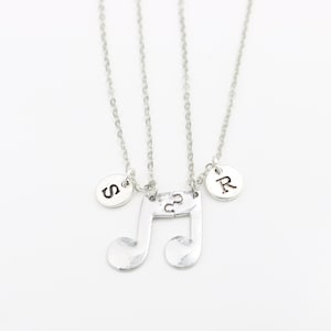 Può includere: Due collane d'argento con un ciondolo a forma di nota musicale e ciondoli con iniziali. I ciondoli con iniziali sono 'S' e 'R'.