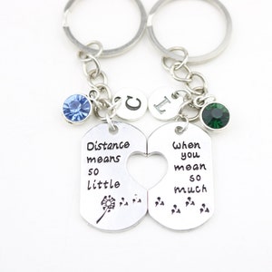 May include: Two silver keychains with a heart-shaped cutout. The left keychain has a blue rhinestone and says "Distance means so little". The right keychain has a green rhinestone and says "When you mean so much".