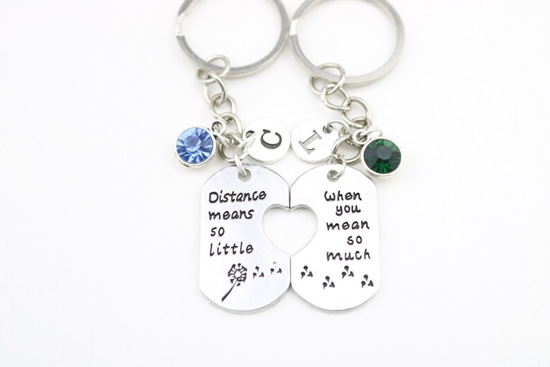 May include: Two silver keychains with a heart-shaped cutout. The left keychain has a blue rhinestone and says "Distance means so little". The right keychain has a green rhinestone and says "When you mean so much".