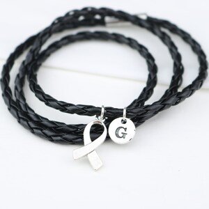 May include: A black leather braided bracelet with a silver ribbon charm and a silver charm with the letter "G" engraved on it.