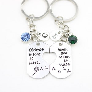 May include: Two silver keychains with a heart-shaped cutout. The left keychain has a blue rhinestone, a dandelion, and the text "Distance means so little". The right keychain has a green rhinestone and the text "When you mean so much".