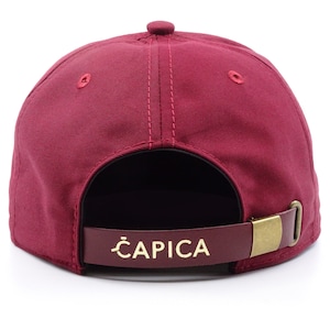 original 5panel burgundy cap with a wooden ziricote palisander visor,on the front is a round logo with our company brand,on the back is a brass buckle with a leather strip on which the company's name is printed,rear view