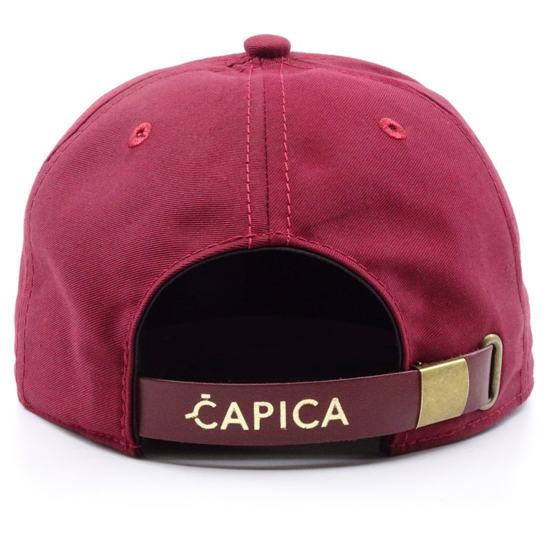 original 5panel burgundy cap with a wooden ziricote palisander visor,on the front is a round logo with our company brand,on the back is a brass buckle with a leather strip on which the company's name is printed,rear view