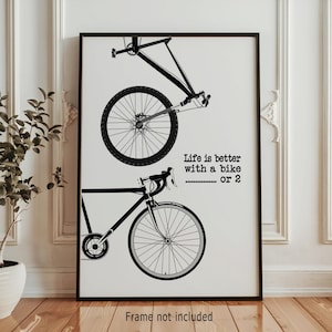 Puede incluir: Lámina artística enmarcada en negro con ilustraciones de dos bicicletas. El texto dice: "La vida es mejor con una bici... o 2."