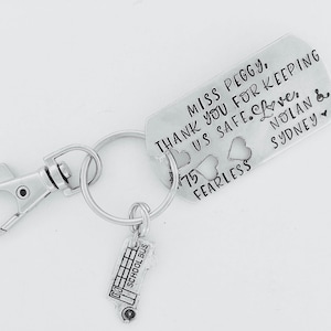 May include: Silver keychain with a school bus charm and a tag that reads "Miss Peggy. Thank you for keeping us safe. Love. Nolan & Sydney. 75 Fearless"