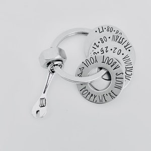 May include: Silver keychain with a wrench charm and three round metal tags. The tags are engraved with the text "Poppy, We're Nuts About You!" "McKenna" and "02.25.17. 08.08.17. TR/STAN - 08-21 100".
