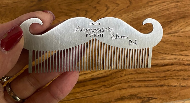 Puede incluir: Un peine de plata en forma de bigote con una inscripci&oacute;n personalizada que dice "Happy Anniversary 07.10.11 Love, Del."