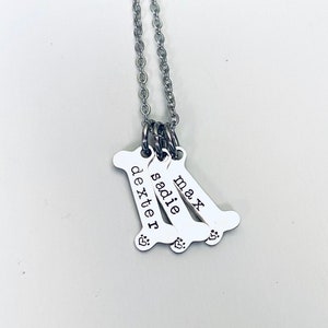 May include: Silver necklace with three bone-shaped charms, each engraved with a different name: Max, Sadie, and Dexter. Each charm has a small paw print.