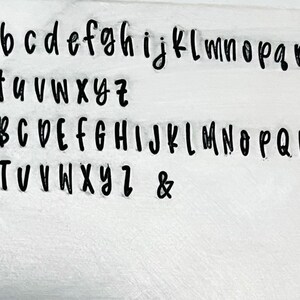 May include: A white surface with a black font showing the alphabet in lowercase and uppercase letters, as well as the ampersand symbol.