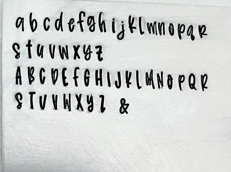 May include: A white surface with a black font showing the alphabet in lowercase and uppercase letters, as well as the ampersand symbol.
