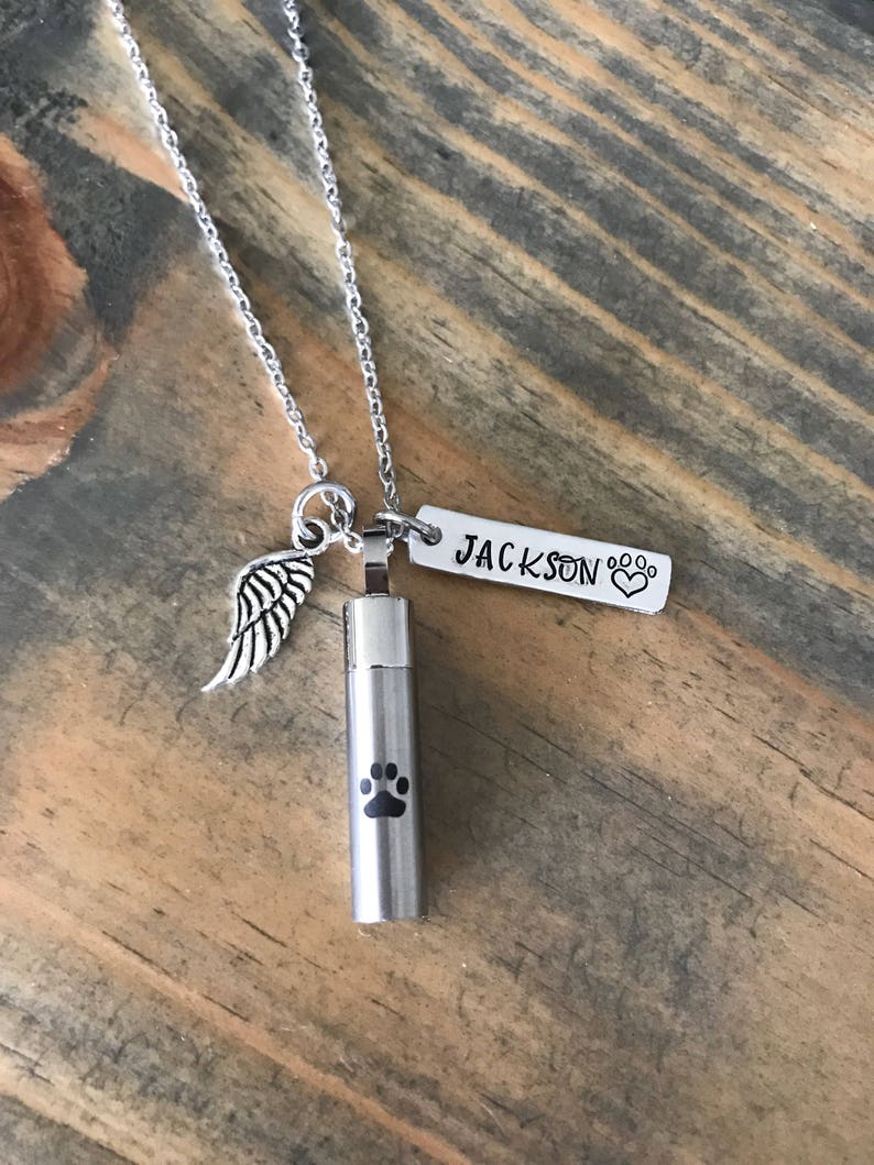 May include: Silver chain necklace with a small silver urn pendant engraved with a paw print. The urn is attached to a silver tag engraved with the name "JACKSON" and a paw print.