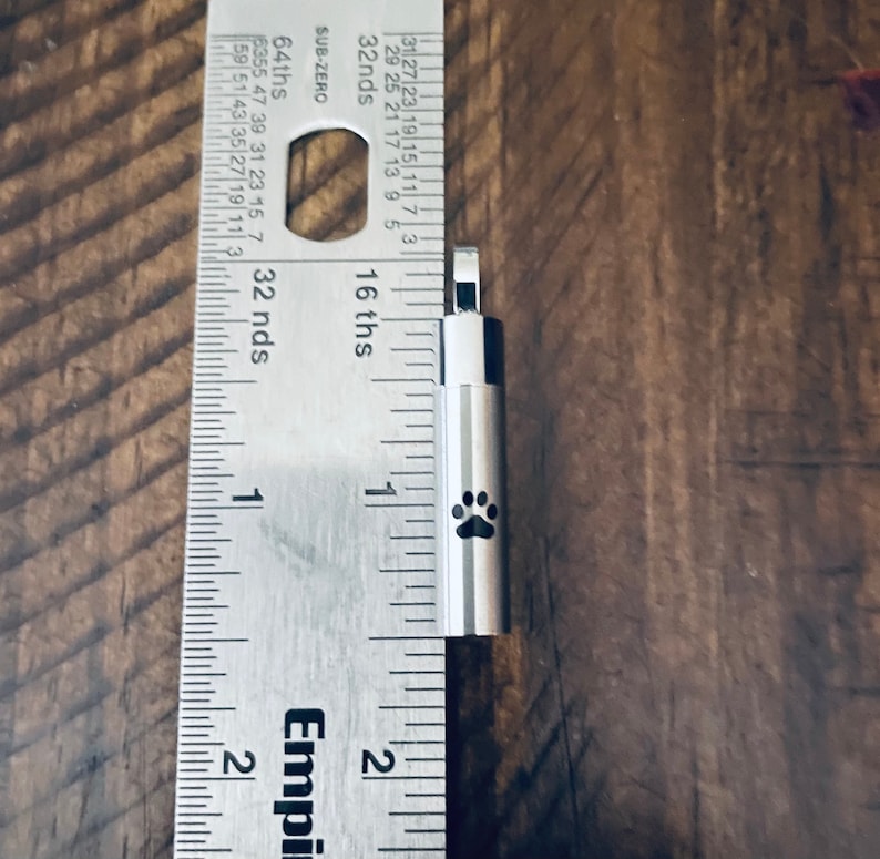 May include: A silver metal keychain with a paw print design. The keychain is about 1 inch long and is measured against a ruler.