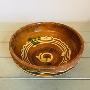 May include: A small, brown ceramic bowl with green and white painted designs. The bowl has a rounded shape and a slightly flared rim.