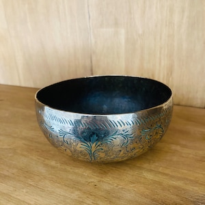 May include: A silver bowl with an intricate floral design etched into the surface. The bowl has a slightly hammered texture and a dark blue interior.
