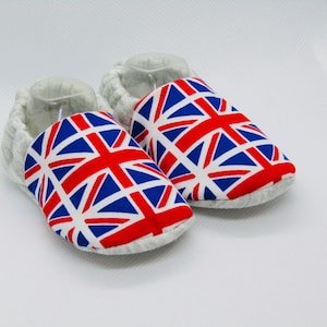 May include: A pair of baby shoes with a Union Jack pattern. The shoes are made of a soft, gray fabric and have a white sole.
