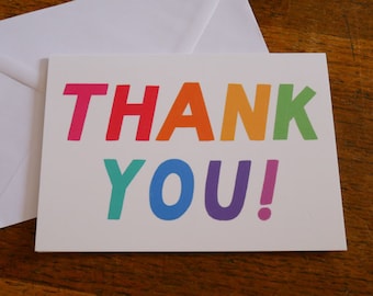 May include: A white card with the words "THANK YOU!" in rainbow colours. The letters are in a bold, playful font.