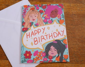 Puede incluir: Una tarjeta de cumpleaños con fondo azul y flores de colores. La tarjeta presenta a tres mujeres con diferentes peinados y tonos de piel. El texto "Happy Birthday" está escrito en un bocadillo.