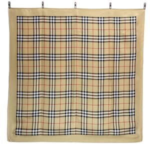 May include: A tan scarf with a classic plaid pattern in black, red, and white. The scarf has a solid tan border and is held up by clips. The design is a timeless fashion accessory.
