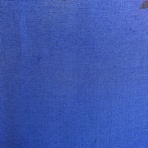 May include: A close-up of a blue fabric with a textured weave. The fabric has a subtle pattern of black, yellow, and pink.