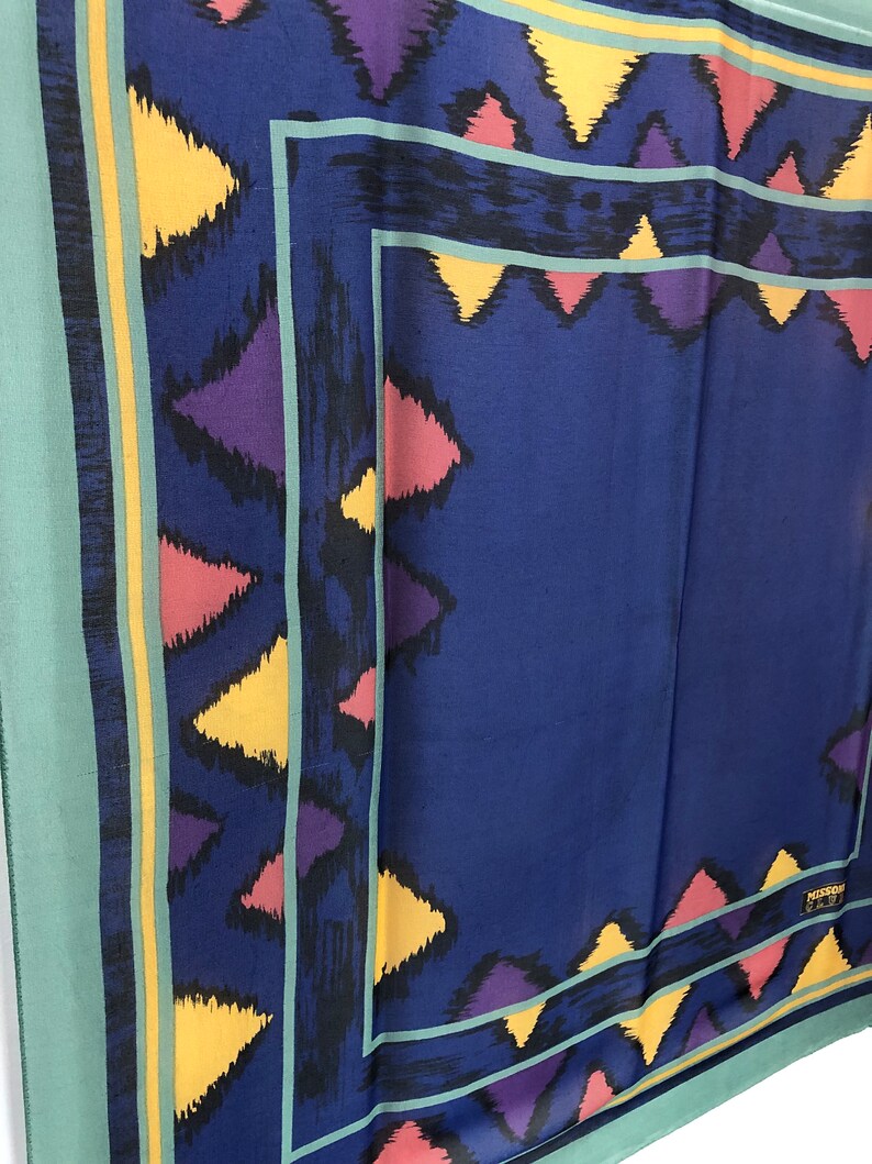 May include: A blue silk scarf with a geometric pattern in shades of yellow, pink, purple, and black. The scarf has a green border and a small label that reads "MISSONI ITALY".
