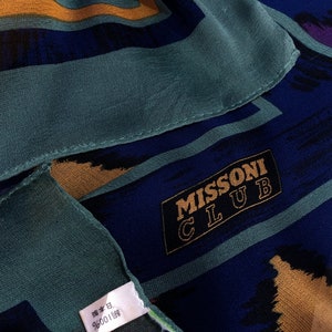 May include: A blue and gold patterned silk scarf with the text "MISSONI CLUB" in a black rectangle. The scarf has a green tag with Japanese text.