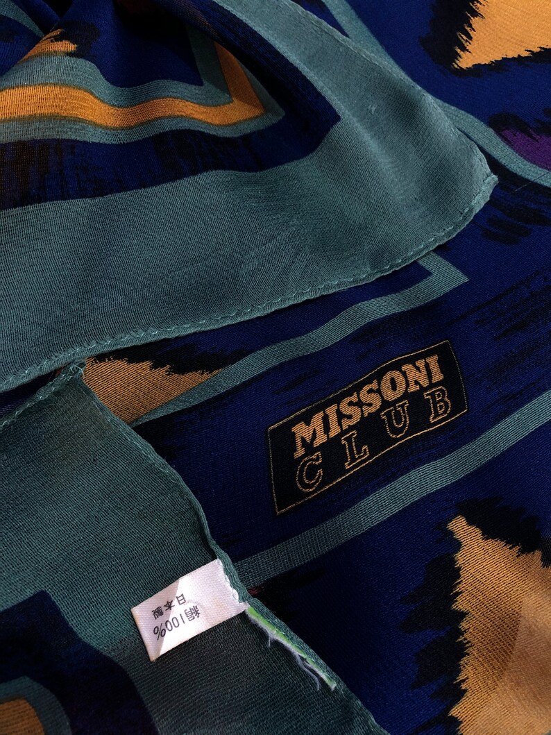 May include: A blue and gold patterned silk scarf with the text "MISSONI CLUB" in a black rectangle. The scarf has a green tag with Japanese text.
