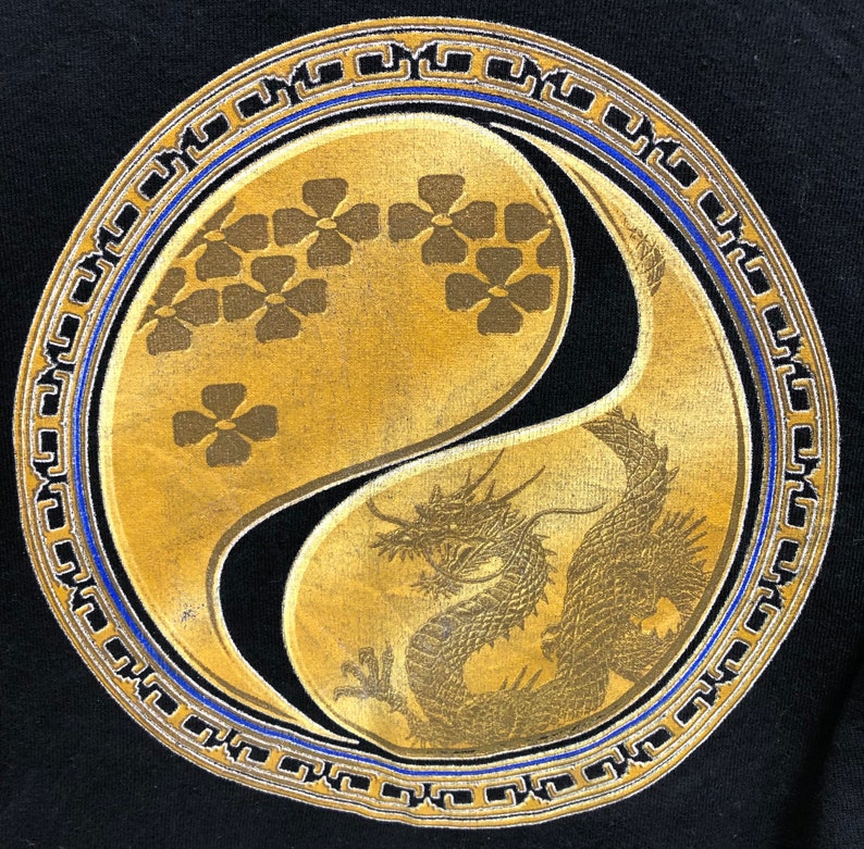 Puede incluir: Un s&iacute;mbolo yin yang dorado con un drag&oacute;n en un lado y flores estilizadas en el otro. El s&iacute;mbolo est&aacute; rodeado por un borde azul y dorado.