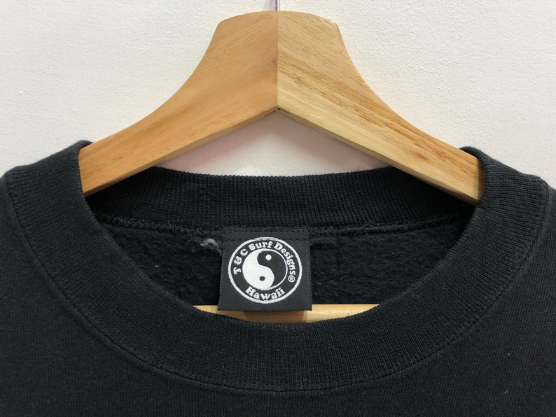 Puede incluir: Sudadera negra con un logotipo redondo de yin yang blanco y negro que dice "T.Y.C. Surf Designs Hawaii".
