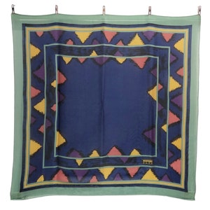 May include: A blue and green patterned silk scarf with a geometric design. The scarf has a border of yellow, pink, and purple triangles. The center of the scarf is a solid blue color. The scarf has the text "MISSOMA" in the bottom right corner.