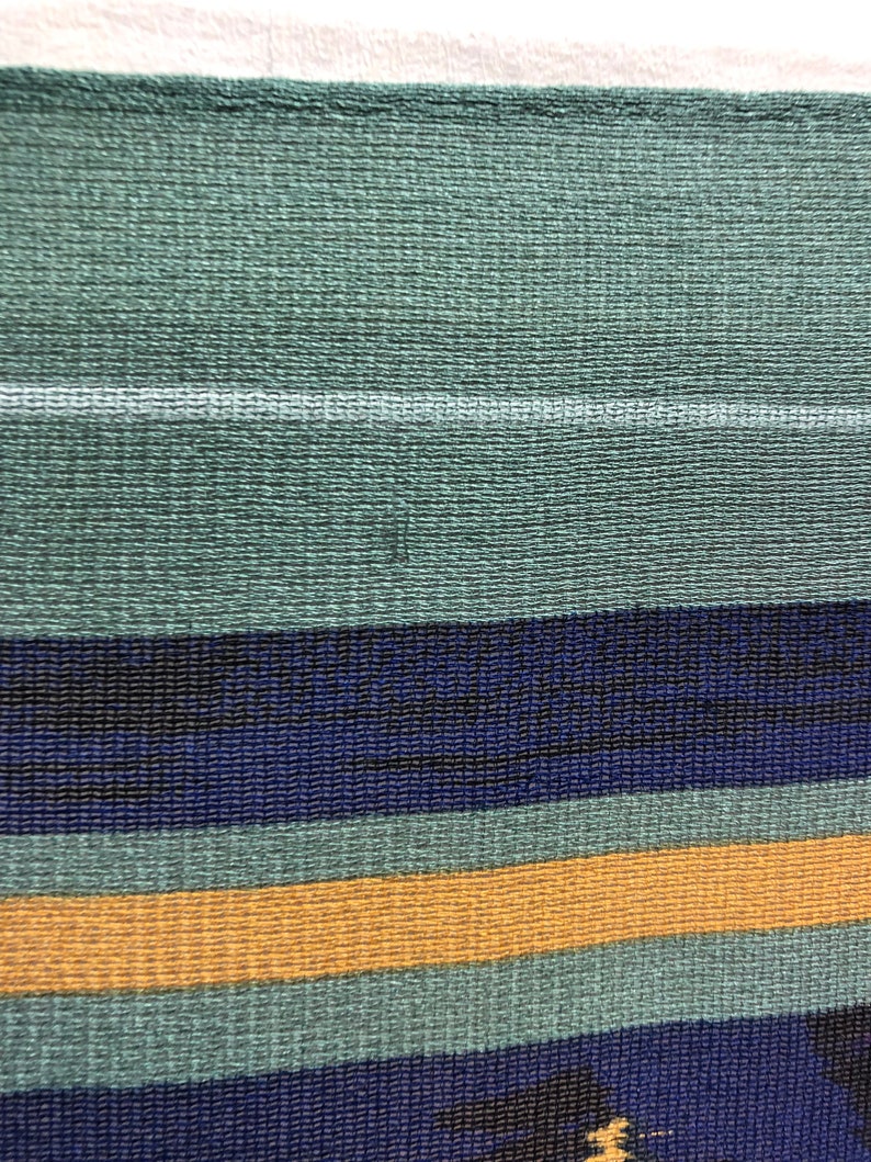 May include: A close-up of a woven fabric with horizontal stripes in shades of green, blue, and yellow.