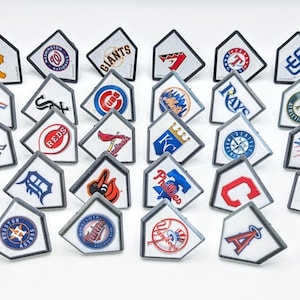 May include: A set of 30 baseball team logos, each printed on a white, diamond-shaped base with a black border. The logos represent different teams from Major League Baseball, including the New York Yankees, Boston Red Sox, and Chicago Cubs.