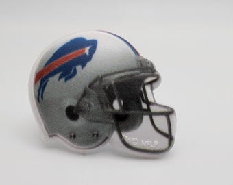 May include: A miniature football helmet pin featuring the Buffalo Bills logo. The helmet is primarily silver with a blue and red logo on the side. The face mask is black, and the pin has the NFLP logo.