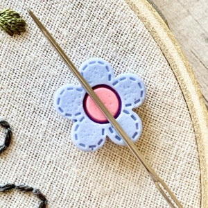 Daisy needle minder magnet holding a sewing needle for embroidery, cross stitch, and needlecrafts.