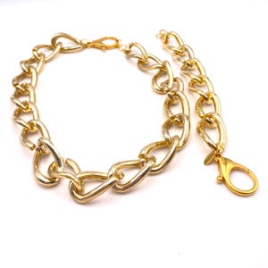 Può includere: Una collana a catena dorata con un design a maglie grandi e spesse. La collana ha una chiusura a moschettone e un'estensione a catena più corta.