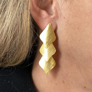 Può includere: Orecchini in oro con un design geometrico a strati. Ogni strato ha una forma di diamante con una finitura spazzolata.