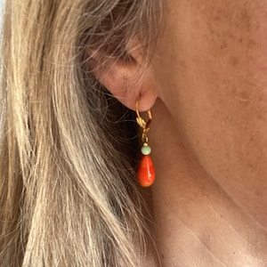Può includere: Orecchini a cerchio dorati con un pendente di corallo e una perla verde. La perla di corallo ha la forma di una lacrima.