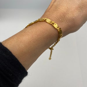 Peut inclure: Un bracelet en chaîne dorée avec un motif délicat et entrelacé. Le bracelet a un fermoir réglable.