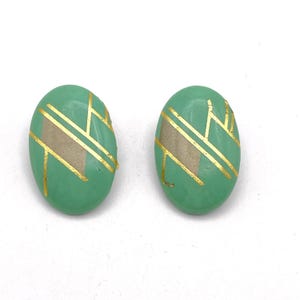 May include: A pair of oval-shaped earrings with a green background and gold geometric designs.