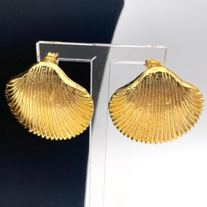 Peut inclure: Une paire de boucles d'oreilles en forme de coquille de couleur or. Les boucles d'oreilles sont en métal et ont une surface texturée.