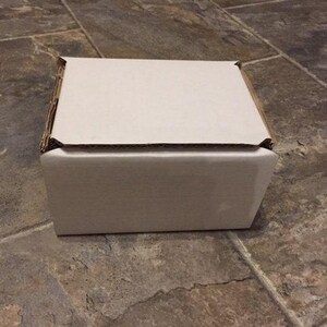 A white cardboard box sits on a tiled floor.