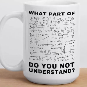 Può includere: Tazza in ceramica bianca con la scritta nera "WHAT PART OF DO YOU NOT UNDERSTAND?" e formule matematiche. La tazza ha un manico grande ed è appoggiata su una superficie di legno.
