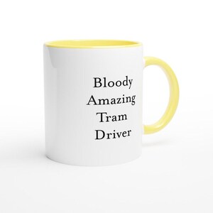 May include: White ceramic mug with a yellow interior and handle. The mug features the text "Bloody Amazing Tram Driver" in black, a humorous and bold statement. Ideal for tea, coffee, or any preferred drink.